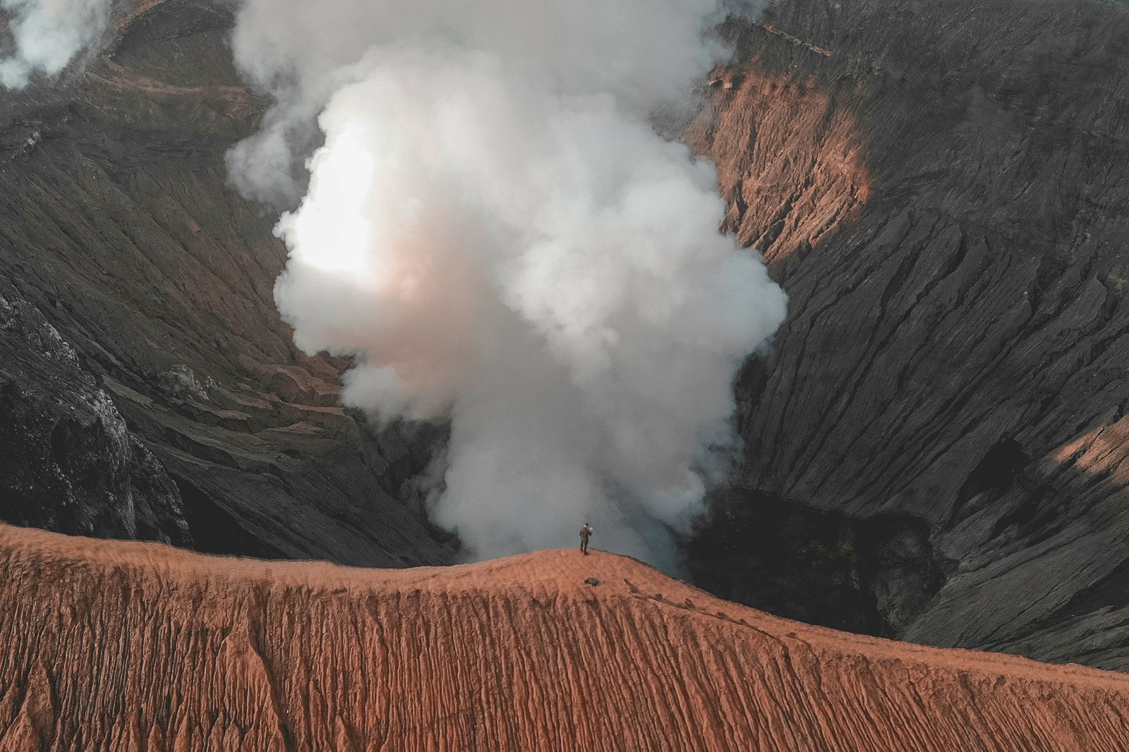 A traveler stands at the edge of Mount Bromo’s smoking crater in Indonesia.